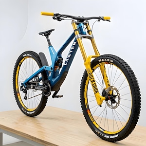 K&ouml;nnte beinhalten: Blau-gelbes Canyon Mountainbike mit schwarzen Reifen. Das Fahrrad hat gelbe Federgabeln und einen Lenker. Die R&auml;der haben gelbe Akzente und die Reifen sind mit dem Namen Maxxis versehen. F&uuml;r Downhill-Fahrten konzipiert.