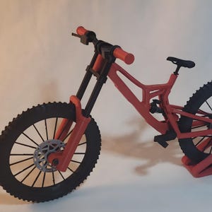 K&ouml;nnte beinhalten: Ein rotes und schwarzes Mountainbike mit schwarzem Sattel und Reifen. Das Fahrrad hat eine Federgabel und Scheibenbremsen. Der Lenker ist rot, und die R&auml;der haben einen Durchmesser von etwa 66 cm.