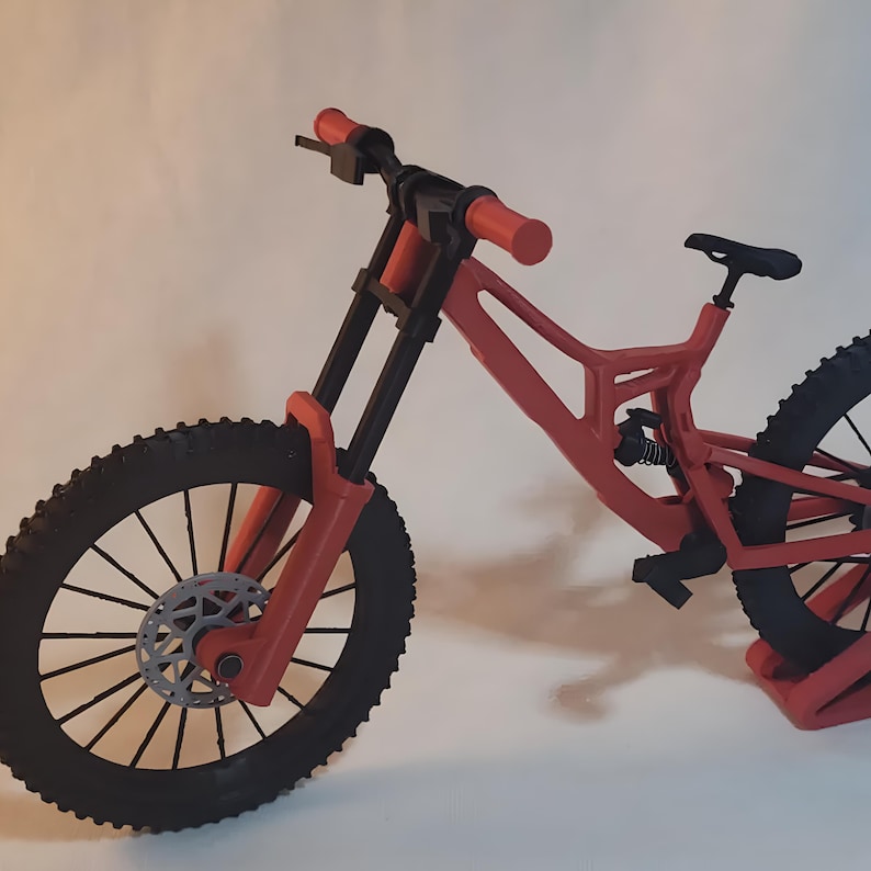 K&ouml;nnte beinhalten: Ein rotes und schwarzes Mountainbike mit schwarzem Sattel und Reifen. Das Fahrrad hat eine Federgabel und Scheibenbremsen. Der Lenker ist rot, und die R&auml;der haben einen Durchmesser von etwa 66 cm.