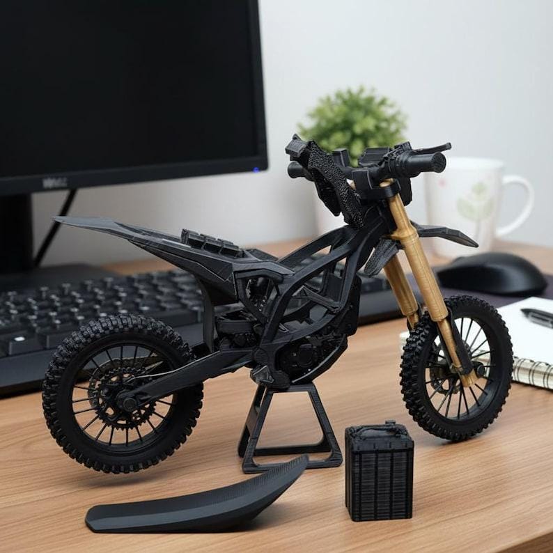 K&ouml;nnte beinhalten: Ein schwarzes Motorradmodell mit goldfarbenen Vorderradgabeln und schwarzen Reifen. Das Modell wird auf einer Holzoberfl&auml;che mit Tastatur, Computermonitor und einer kleinen Pflanze im Hintergrund ausgestellt. Zus&auml;tzliche Teile sind in der N&auml;he des Modells platziert.