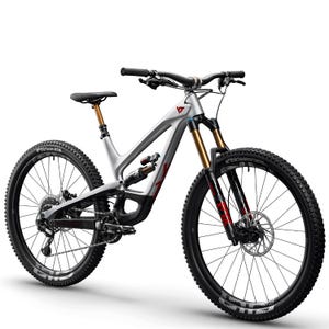 Könnte beinhalten: Ein silbernes Mountainbike mit schwarzen Reifen und einem schwarzen Lenker. Das Fahrrad hat goldene Federgabeln und rote Akzente. Die Reifen haben ein Stollenprofil und das Fahrrad steht vor einem weißen Hintergrund.