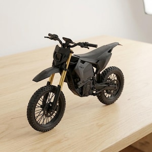 Puede incluir: Una maqueta de motocicleta negra y dorada con neum&aacute;ticos de tacos, un faro y un manillar. La motocicleta tiene un dise&ntilde;o elegante y est&aacute; sobre una superficie de madera. El texto "SPAM 31" es visible en el lateral de la motocicleta.