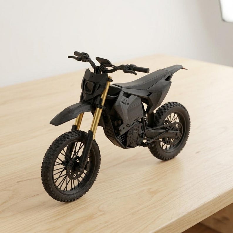 Puede incluir: Una maqueta de motocicleta negra y dorada con neum&aacute;ticos de tacos, un faro y un manillar. La motocicleta tiene un dise&ntilde;o elegante y est&aacute; sobre una superficie de madera. El texto "SPAM 31" es visible en el lateral de la motocicleta.