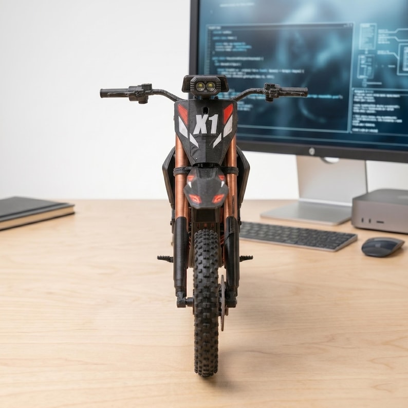 May include: A black and copper-colored toy motorcycle with the text "X1" on the front. The motorcycle has a black tire and is sitting on a wooden surface. The background includes a computer monitor, keyboard, and mouse.