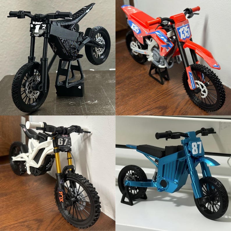 Puede incluir: Cuatro motocicletas de juguete en miniatura de varios colores. Una es negra, otra roja con detalles azules, una tercera blanca con horquillas doradas y la &uacute;ltima azul. Cada una tiene un dise&ntilde;o &uacute;nico y se exhibe sobre un soporte.