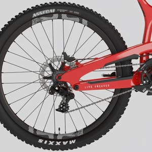 May include: Close-up of a red mountain bike frame and rear wheel. The black tire has white lettering and a knobby tread. The frame has the words "LIVE UNCAGED" printed on it. The wheel has silver spokes and a disc brake.