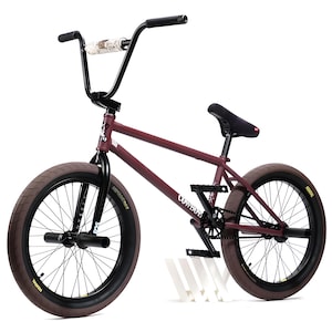 May include: A maroon BMX bike with black handlebars and a black seat. The tyres are brown with black rims. The bike has the word "Cowboy" printed on the frame.