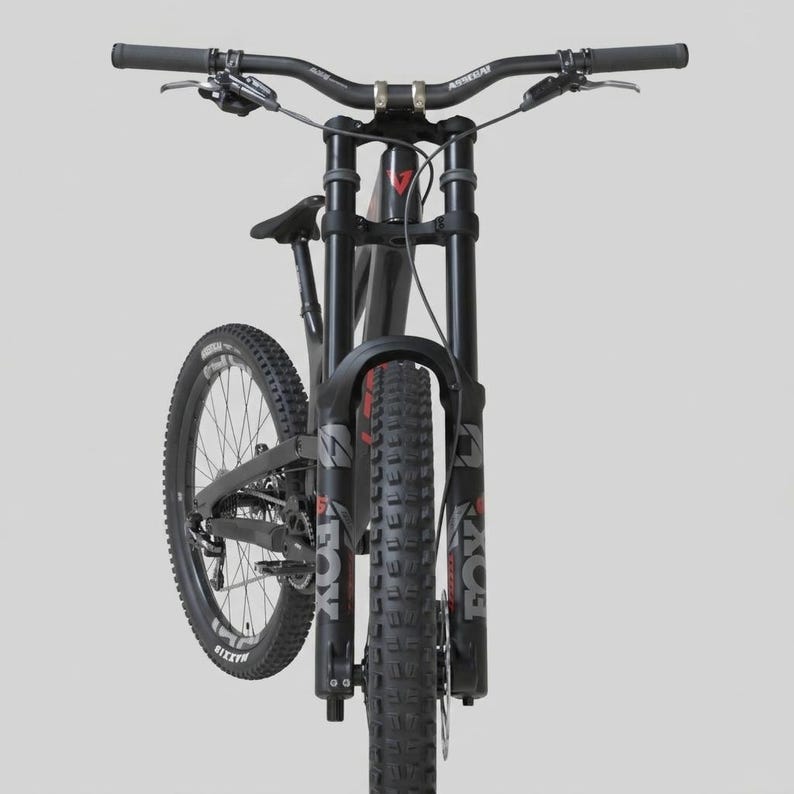 May include: A black mountain bike with a suspension fork and wide handlebars. The tires are thick and knobby, designed for off-road use. The bike has the brand name "FOX" printed on the front suspension.