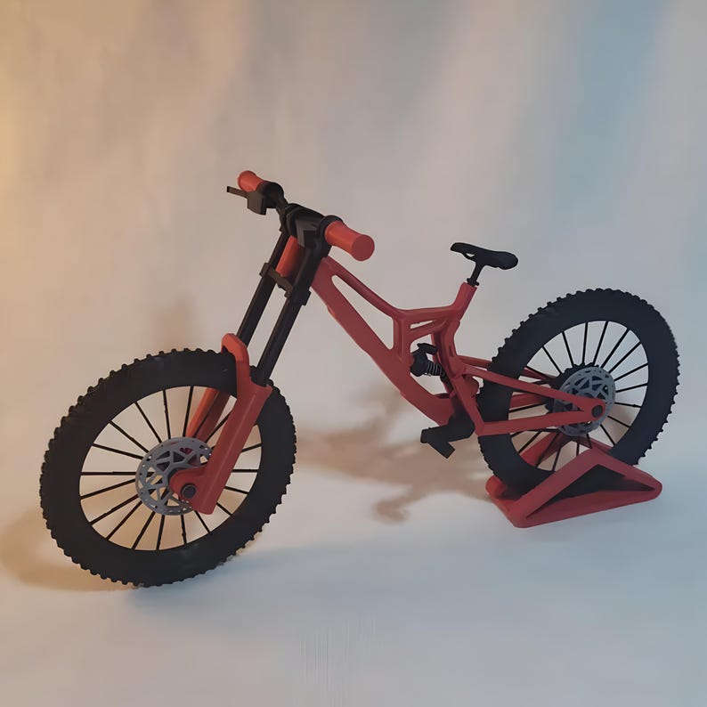 K&ouml;nnte beinhalten: Ein rotes und schwarzes Mountainbike-Modell mit detailliertem Design. Das Fahrrad hat schwarze Reifen, einen schwarzen Sattel und rote Lenker. Der Rahmen ist rot und die R&auml;der haben ein komplexes Speichenmuster. Das Fahrrad wird vor wei&szlig;em Hintergrund gezeigt.