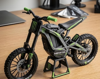 May include: A black and green toy motorcycle with the Monster Energy logo. The model has green accents on the handlebars, frame, and wheels. The tires are black with a tread pattern, and the motorcycle is on a black stand.