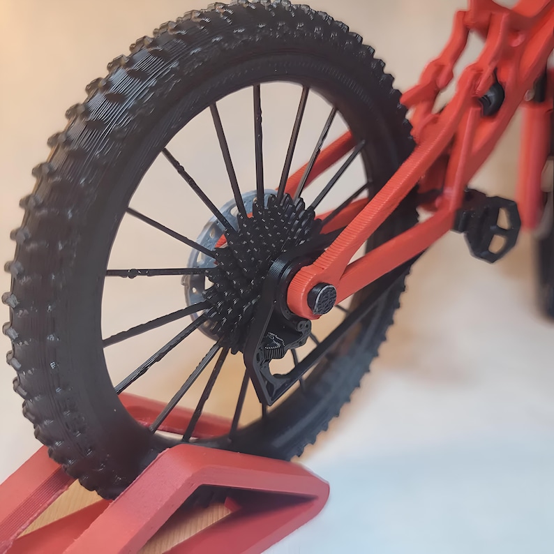 K&ouml;nnte beinhalten: Nahaufnahme eines roten und schwarzen Mountainbike-Modells. Der schwarze Reifen hat ein profiliertes Profil. Der Rahmen und die Komponenten des Fahrrads sind rot. Das Hinterrad ist sichtbar, mit Kassette und Scheibenbremse.
