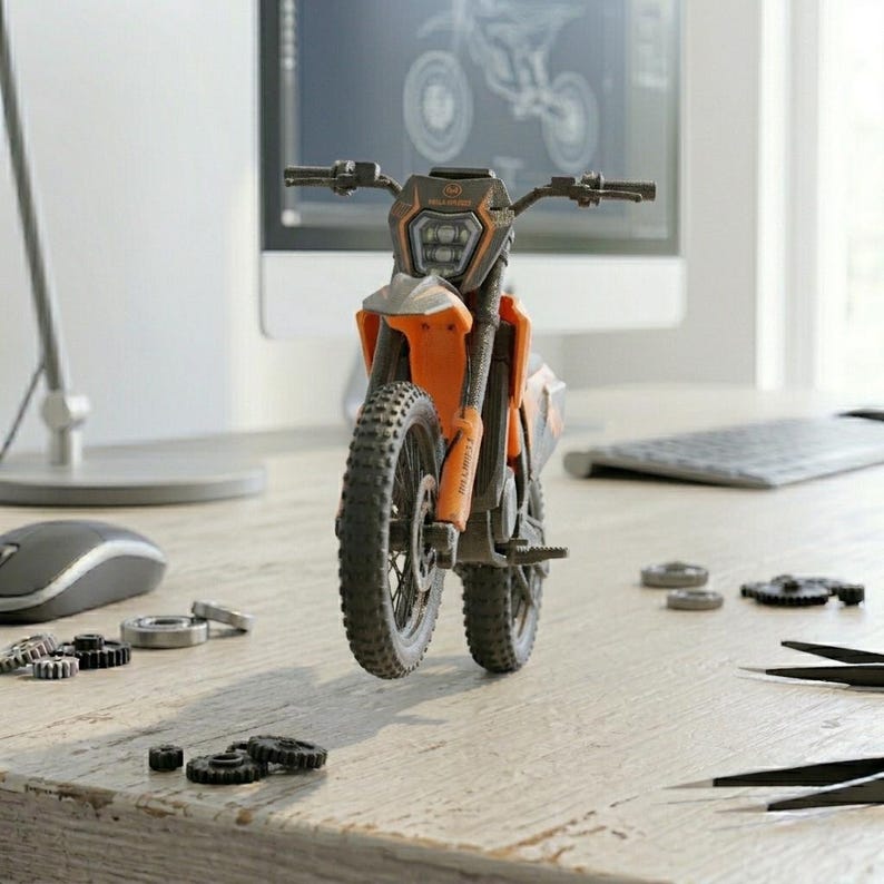 May include: An orange and black toy motorcycle with a detailed design, featuring a front headlight and knobby tires. The motorcycle is positioned on a wooden surface, with small mechanical parts scattered around it. A computer monitor is in the background.
