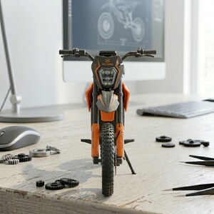 May include: An orange and black toy motorcycle with the word "HILLBILLY" on the front. The motorcycle is on a wooden desk with computer parts and a computer monitor in the background.
