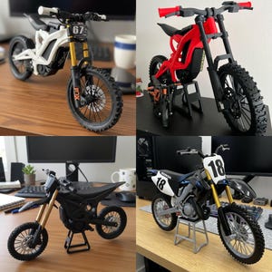 May include: Four miniature dirt bikes in white, red, black, and black and blue. Each bike has a unique design, with details like number plates, suspension forks, and knobby tires. The bikes are displayed on stands, showcasing their features.