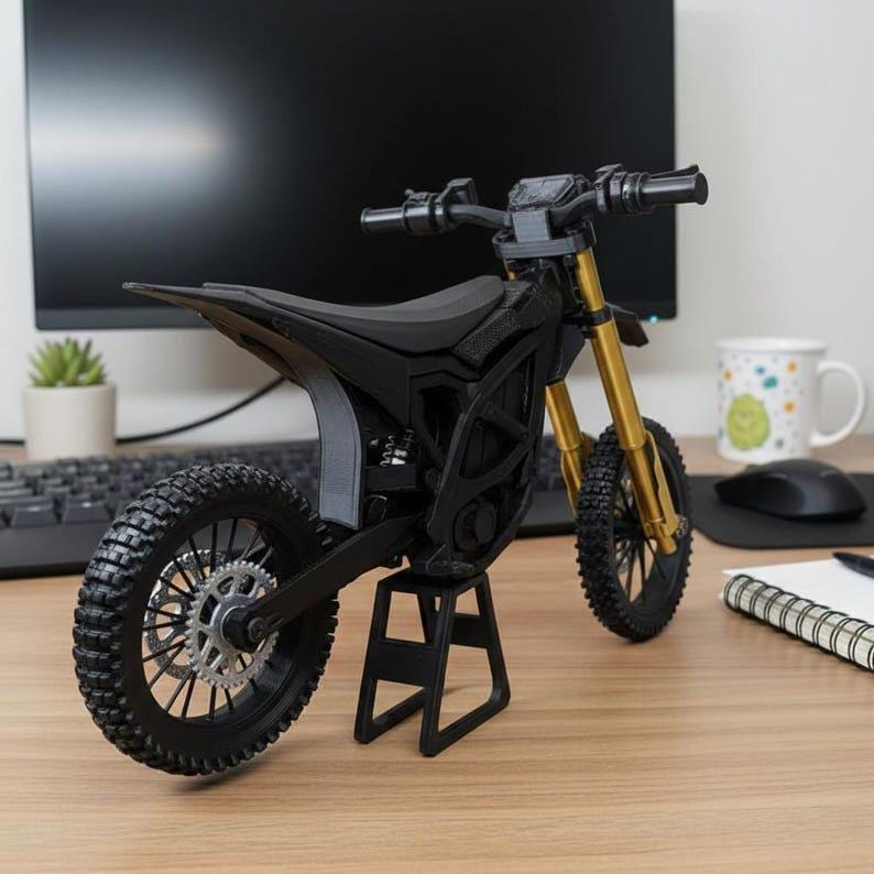 May include: A black and gold miniature motorcycle model with a detailed design. The model has a black frame, seat, and tires, with gold-colored front forks. It is displayed on a black stand, showcasing the intricate details of the motorcycle.