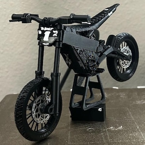 May include: A black miniature motorcycle with a number 1 on the front. The motorcycle has a sleek design with black tires, a black frame, and a black seat. The motorcycle is on a black stand.