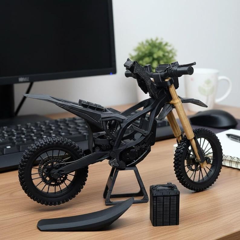 Puede incluir: Una maqueta de motocicleta negra y beige con un dise&ntilde;o detallado. El modelo incluye un asiento, ruedas y un soporte. La motocicleta se exhibe sobre una superficie de madera.