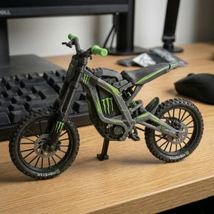 May include: A miniature black and gray motorcycle model with green accents and the "Monster" logo. The model features a detailed design, including wheels, handlebars, and a seat. The handlebars are green. The model is displayed on a wooden surface.