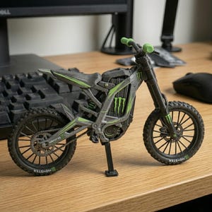 May include: A detailed model of a gray and black motorcycle with green accents. The motorcycle features the "Monster" logo and is set on a wooden surface. The handlebars and wheels are black, and the tires have a textured design.