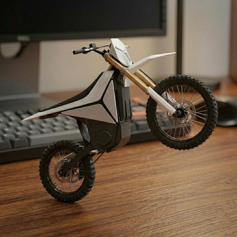 Op de afbeelding: Een moderne motorfiets met een futuristische uitstraling, in een wit en zwart kleurenschema. De motorfiets heeft een strak ontwerp met een omhooggeheven voorwiel, wat zijn offroad-capaciteiten benadrukt. De banden zijn zwart met een noppenprofiel.