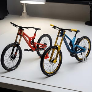 Op de afbeelding: Twee miniatuur mountainbike modellen. De ene is een rode Santa Cruz fiets met een zwart stuur en zwarte banden. De andere is een blauwe Canyon fiets met een gele voorvork, gele handvatten en zwarte banden met gele velgen.