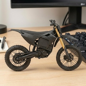 Puede incluir: Una motocicleta negra en miniatura con horquillas delanteras doradas. El modelo tiene neum&aacute;ticos detallados, un asiento y una cadena visible. El texto "501-99913" est&aacute; impreso en el lateral. La motocicleta se exhibe en un escritorio.