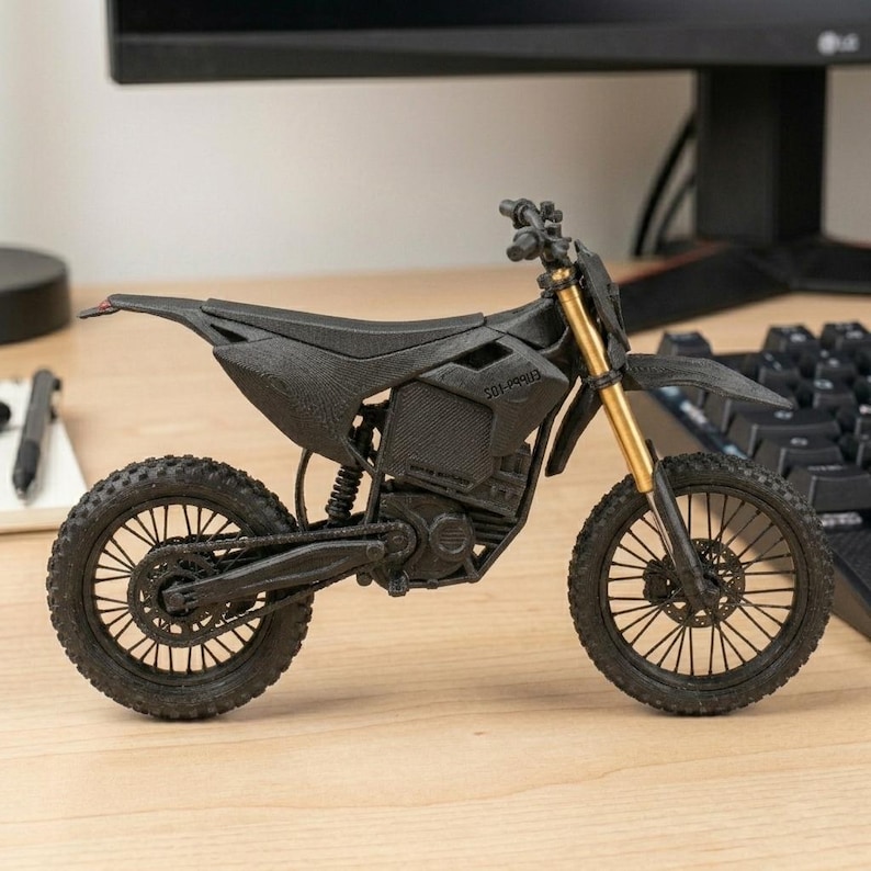Puede incluir: Una motocicleta negra en miniatura con horquillas delanteras doradas. El modelo tiene neum&aacute;ticos detallados, un asiento y una cadena visible. El texto "501-99913" est&aacute; impreso en el lateral. La motocicleta se exhibe en un escritorio.