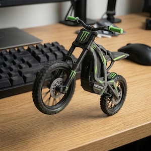 May include: A black and green toy motorcycle with the Monster Energy logo. The toy motorcycle has green accents on the frame, handlebars, and wheels. The tires are black and have a tread pattern. The motorcycle is on a wooden surface.