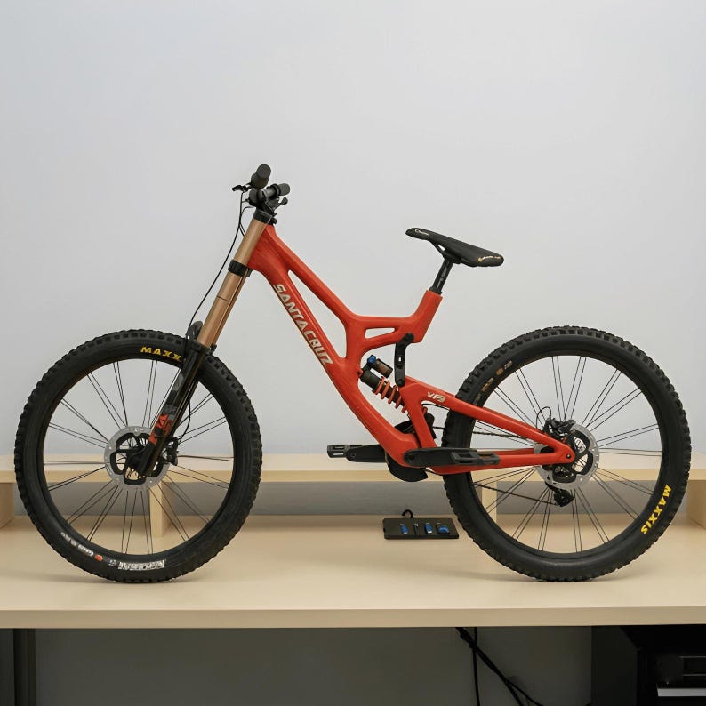 May include: A red Santa Cruz V10 mountain bike with a full suspension frame, black handlebars, black tires with yellow Maxxis lettering, a black seat, and a rear shock absorber. The frame features the Santa Cruz brand name in white lettering.