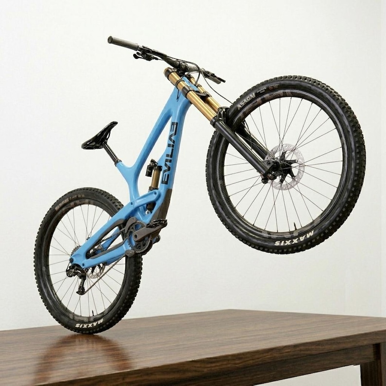 May include: A light blue mountain bike with black tires and gold suspension forks. The bike has the word "EVIL" printed on the frame. The bike is positioned with the front wheel raised, showcasing its design and components.