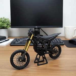 K&ouml;nnte beinhalten: Ein detailliertes Miniatur-Motorradmodell in Schwarz und Gold. Das Modell hat einen schwarzen Rahmen, Reifen und Sitz, mit goldfarbenen Vorderradgabeln. Es wird auf einem Holzschreibtisch ausgestellt, um sein aufwendiges Design und seine Konstruktion hervorzuheben.