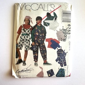 Può includere: Una busta di cartamodello vintage McCall's con illustrazioni di abbigliamento per bambini. Il modello include tute, una felpa con cappuccio, magliette e accessori. La busta presenta il logo McCall's e il numero del modello 6753.