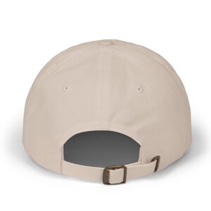 May include: A beige baseball cap with a curved peak. The back of the cap has an adjustable metal buckle. The cap is made of a plain, solid-coloured fabric.