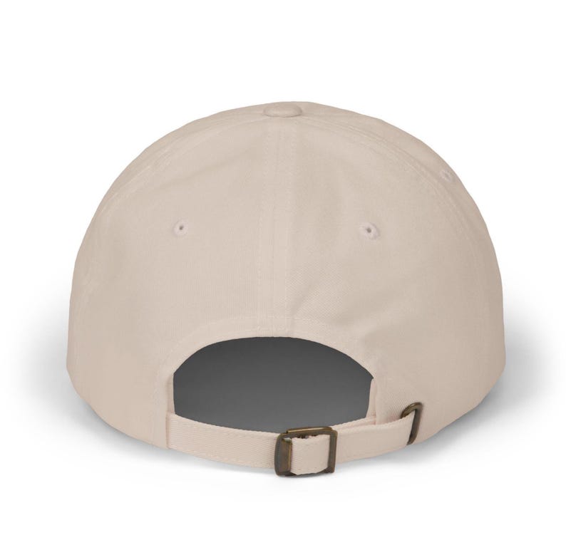 May include: A beige baseball cap with a curved peak. The back of the cap has an adjustable metal buckle. The cap is made of a plain, solid-coloured fabric.