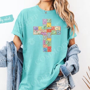 Puede incluir: Una camiseta turquesa con un dise&ntilde;o de cruz hecho de cuadrados de patchwork floral. Las palabras "chalky mint" est&aacute;n escritas en una fuente azul claro en la parte superior izquierda. La camiseta tiene mangas cortas y un corte holgado.