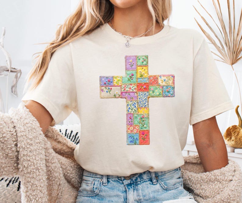 Puede incluir: Camiseta color crema con un dise&ntilde;o de cruz colorida. La cruz est&aacute; hecha de peque&ntilde;os parches cuadrados con estampados florales en varios colores, incluyendo rosa, azul, amarillo y verde. La camiseta se combina con vaqueros azules.