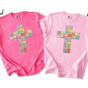Puede incluir: Dos camisetas de manga corta, una rosa ne&oacute;n y otra rosa claro, cada una con un dise&ntilde;o de cruz. La cruz est&aacute; compuesta por cuadrados coloridos de estilo patchwork con estampados florales. La camiseta rosa ne&oacute;n tiene el texto "neon pink" y la rosa claro tiene el texto "blossom".