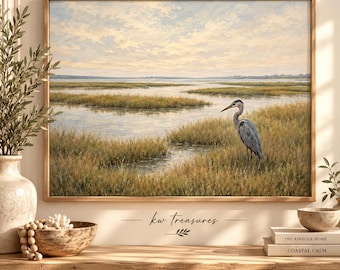 May include: A framed landscape painting depicting a grey heron standing in a marshy wetland with tall golden grasses and calm water under a soft, cloudy sky. The text "kw treasures" is printed in black below the center of the artwork.