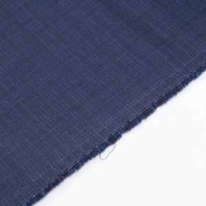May include: A close-up of a piece of navy blue fabric with a textured weave. The fabric is cut at an angle, revealing a raw edge with loose threads. The background is plain white, highlighting the rich color and texture of the textile.