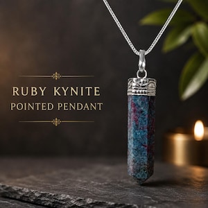 Puede incluir: Un colgante de rubí cianita en forma de punta con cadena de plata. La piedra cilíndrica presenta inclusiones minerales en azul profundo y rojo magenta. La parte superior del cristal está engastada en una tapa de plata. Texto: RUBY KYNITE POINTED PENDANT.