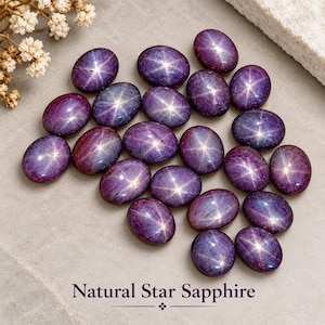 May include: A collection of oval-shaped, deep purple natural star sapphires, each displaying a distinct six-rayed star pattern on its polished surface. The text Natural Star Sapphire is printed at the bottom of the image in dark purple font.