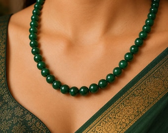 May include: A single-strand necklace composed of uniform, smooth, spherical dark green beads. The beads have a polished, reflective surface and are strung together in a continuous circular arrangement that rests around the base of the neck.