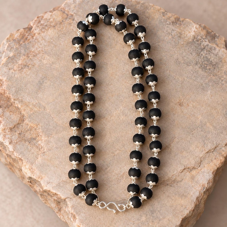 May include: A double-strand necklace featuring matte black spherical beads, each accented with small silver-toned metal caps at the top and bottom. The strands are connected by a silver-toned metal S-hook clasp at the base of the necklace.