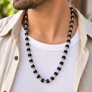 May include: A necklace featuring a series of matte black spherical beads connected by polished silver-toned metal links. The beads are uniform in size and arranged in a continuous strand that rests around the neck, creating a distinct contrast.