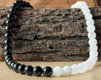 May include: A bracelet made of black and white beads. The beads are round and strung together. The bracelet is displayed on a piece of wood with a textured surface.