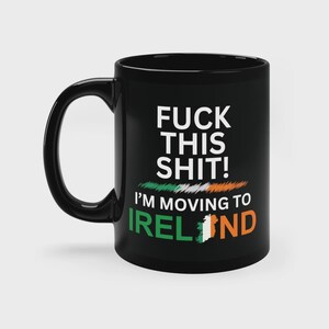 May include: A black ceramic mug featuring the white text FUCK THIS SHIT! I'M MOVING TO IRELAND. The design includes a brushstroke graphic in the colors of the Irish flag and a map of Ireland replacing the letter A in the word IRELAND.