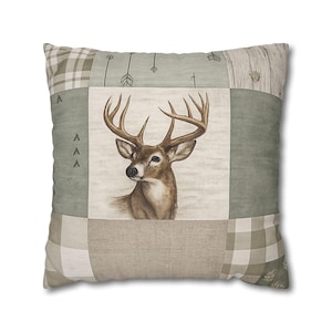 Puede incluir: Cojín decorativo cuadrado con diseño de patchwork. El centro presenta una ilustración detallada de un ciervo con grandes astas. Los parches circundantes incluyen patrones de cuadros, flechas y vetas de madera en tonos verdes, beige y blanco.