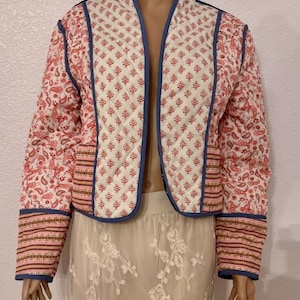 May include: A quilted jacket with a white background and a red floral pattern. The jacket has a blue trim and a striped pattern on the cuffs. The jacket is open in the front.