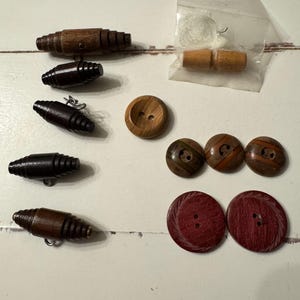Könnte beinhalten: Verschiedene Holzknöpfe und Knebel in verschiedenen Brauntönen. Enthält runde Knöpfe, tonnenförmige Knebel und einen Knopf mit zwei Löchern. Einige Knöpfe haben dekorative Details.