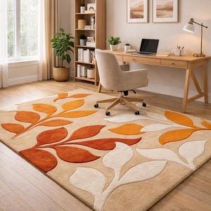 May include: Beige area rug with a leaf design in shades of orange and white. The rug is in a home office setting with a wooden desk, chair, and bookshelf. The room has a window with beige curtains.
